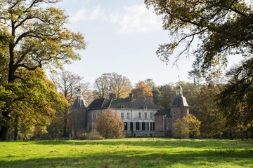 Fototapeta na wymiar Castle in autumn landscape with large trees and meadow. Dutch old estate monumental building in fall natural park. Historic locations. Travel destination at Gelderland in the Netherlands. 