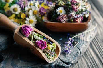 medicinal herbal tea with chamomile flowers and a bouquet of wild flowers in a wooden scoop on a rustic wooden background. Rustic still life, authentic setting