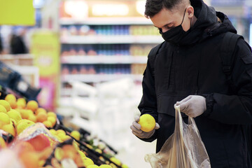 A young man wearing a mask and protective gloves buys food at a store during the coronavirus epidemic.