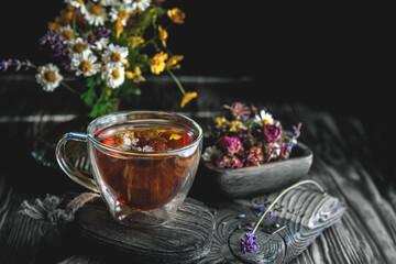 Cup of medicinal herbal tea with chamomile flowers and a bouquet of wild flowers on a rustic wooden background. Rustic still life, authentic setting. Copy space