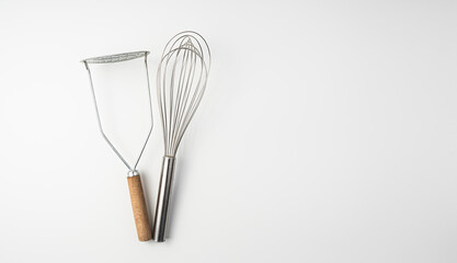 The whisk and the potato masher on white background.Culinary background, top view.