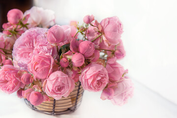 bouquet of pink English roses in a basket on a light table background. Close-up of rose buds, selective focus. Close up