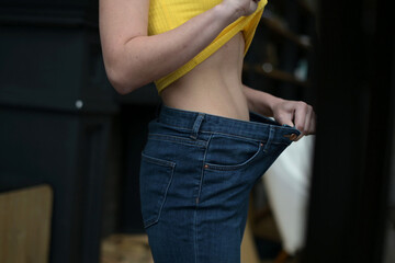 Fototapeta na wymiar Jeans fit loosely on a thinner woman, close up. Woman looks an mirror