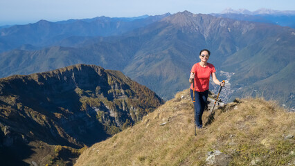 Fototapeta premium Woman hiker goes hiking, stands on top of mountain and looks at autumn nature mountains landscape in sunny weather. Outdoor activities. Copy space