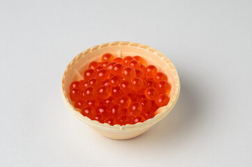 Red caviar tartlets on a white surface with a shadow.