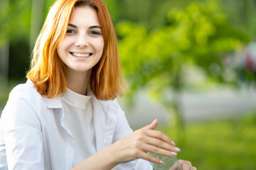 Young happy redhead girl holding water bottle in her hands in summer park.