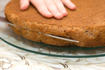 Closeup of female hand holding sharp knife cutting biscuit chocolate cake. Working process of homemade baking.