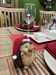 A funny toy hedgehog in a new year's cap stands near a festive plate on a new year's table