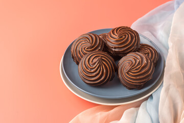 Traditional Russian vanilla marshmallows in chocolate glaze in blue and white plates on pink background. Colorful table and silk textiles