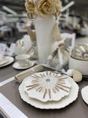 White and gold Christmas star lies on white serving plates standing on a festive table decorated in white colors.