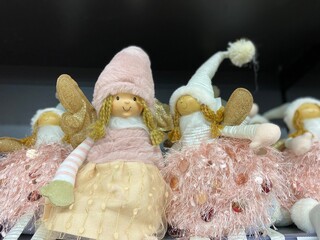 Two dolls with Golden wings in warm clothes sit on a dark background. One doll looks straight and the other looks at the first one. Photo in pastel colors.