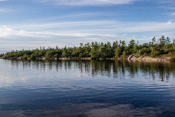 Obraz na płótnie Canvas calm water on the lake with rocky shoreline and evergreen trees at Frying Pan Bay, Beausoleil Island