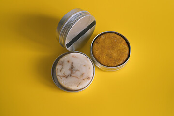 Solid shampoo and soap bars in reusable aluminum jars. Handmade cosmetics, craft cosmetics and home care. The concept of minimalism and reasonable consumption. Yellow background. Selective focus.