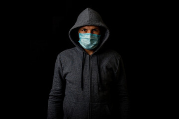Naklejka na ściany i meble Young man in a medical mask in a sweatshirt looking at the camera on a black background.