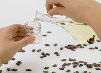 A hand pours watermelon oil into a jar, watermelon seeds are scattered on the table, close-up on a white background