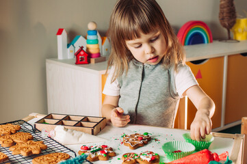 Little girl decorating Christmas gingerbread cookies with sprinkles