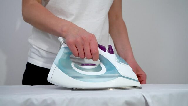 A woman irons clothes with a steam iron on an Ironing Board close-up on a white background. 4K video