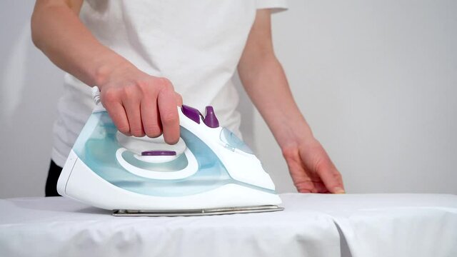 A woman irons clothes with a steam iron on an Ironing Board close-up on a white background. 4K video