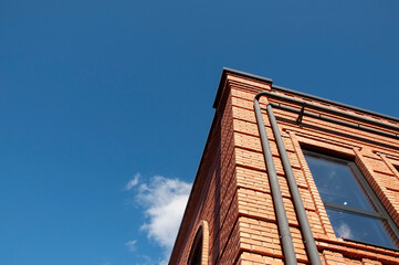 red brick corner of the building in perspective against a blue sky with a cloud on a sunny day