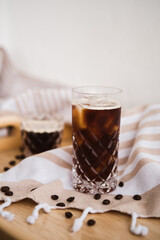 Black ice coffee in the glass on the ligh background, tablecloth with beige stripes, coffee beans
