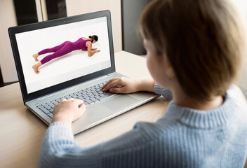 A girl does sports exercises while watching fitness classes on a laptop computer online.