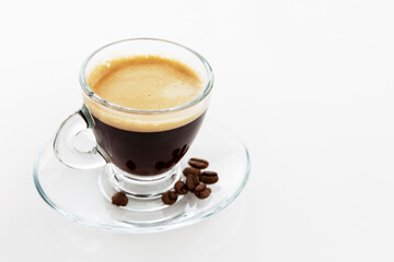 Transparent cup of espresso on a white background. There are coffee beans on the saucer. Space for text.