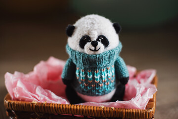 Handmade knitted toy. Amigurumi panda toy in  blue color sweater on the wooden  background. Crochet...