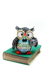 Handmade knitted toy. Amigurumi black owl toy holding mouse and sitting on the book  on the white...