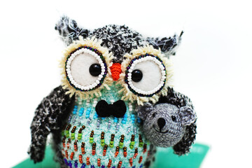 Handmade knitted toy. Amigurumi black owl toy holding mouse and sitting on the book  on the white background. Crochet stuffed animals. 