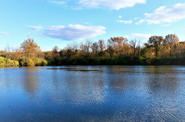 Obraz premium Beautiful autumn landscape with a view of the opposite bank of the river, clouds and trees are reflected in the blue water