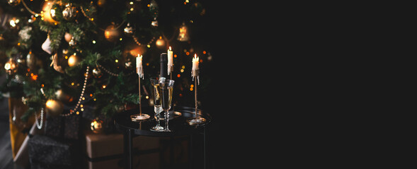 Two glasses and bottle of champagne standing on table with Christmas tree on a background.