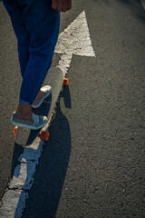Detalle de las piernas y pies de una mujer sobre un skate y una flecha blanca pintada en el suelo 