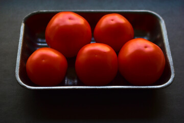 Red ripe tomatoes in a package on a black background