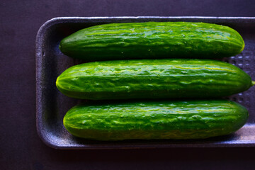 Green ripe cucumbers in a package on a black background
