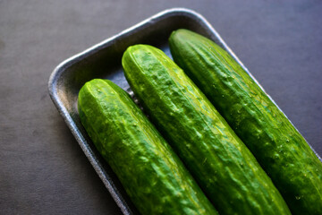 Green ripe cucumbers in a package on a black background