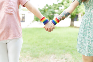Women friends holding hands with rainbow wristbands