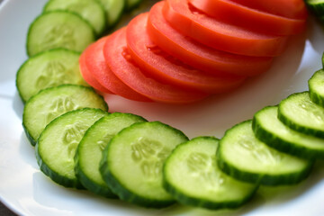 Sliced Green cucumber and tomato on a white plate on a black background