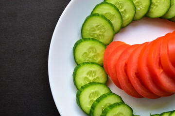 Sliced Green cucumber and tomato on a white plate on a black background