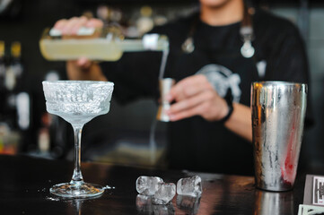Bartender adds drink and ingredients to cocktail glass on bar counter with bar equipment