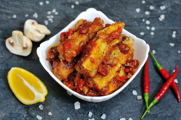 Tasty Bass fish fillets in Mediterranean sauce with tomatoes, olives and capers in baking pan on rustic wooden background with ingredients. Top view