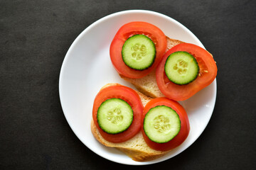 Sandwiches on a white plate with cucumber and tomato on white bread