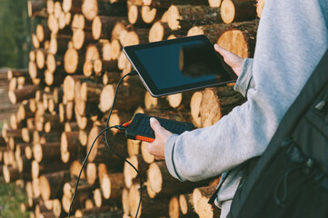 Powerbank, in the hands of a girl with tablets, against the background of timber harvesting.