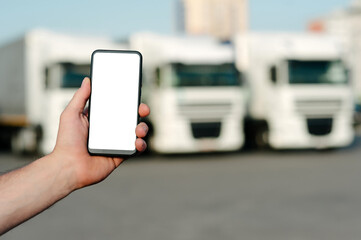 Mock up of a smartphone in a man's hand. Against the backdrop of trucks. Logistics concept.