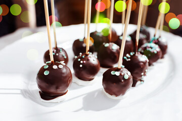 Festive chocolate cake pops with candy sprinkles close-up on the white background. 
Intentional selective focus.