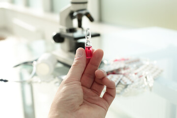 Doctor's hand holding a vaccine in his hands on the background of a glass table with medicines and a microscope