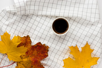 Autumn composition. Cup of coffeecup, autumn leaves on on white checkered cloth. Flat lay, top view, copy space