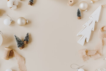Obraz premium Blank frame with mockup copy space made of Christmas toys: fir-trees, baubles, ribbons on pastel beige background. Christmas / New Year celebration decoration. Holiday concept. Top view, flat lay.