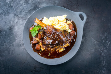 Modern style traditional braised slow cooked lamb shank in red wine sauce with shallots and mashed potatoes offered as top view in a design cast iron plate with copy space © HLPhoto