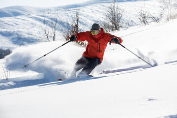 Fototapeta na wymiar A skier is in the deep snow. Sunny winter day. A skier is wearing red jacket. 