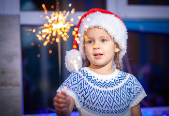 Festive Merry Christmas sparklers. Portrait of a cute little girl holding sparklers, new year 2021,...